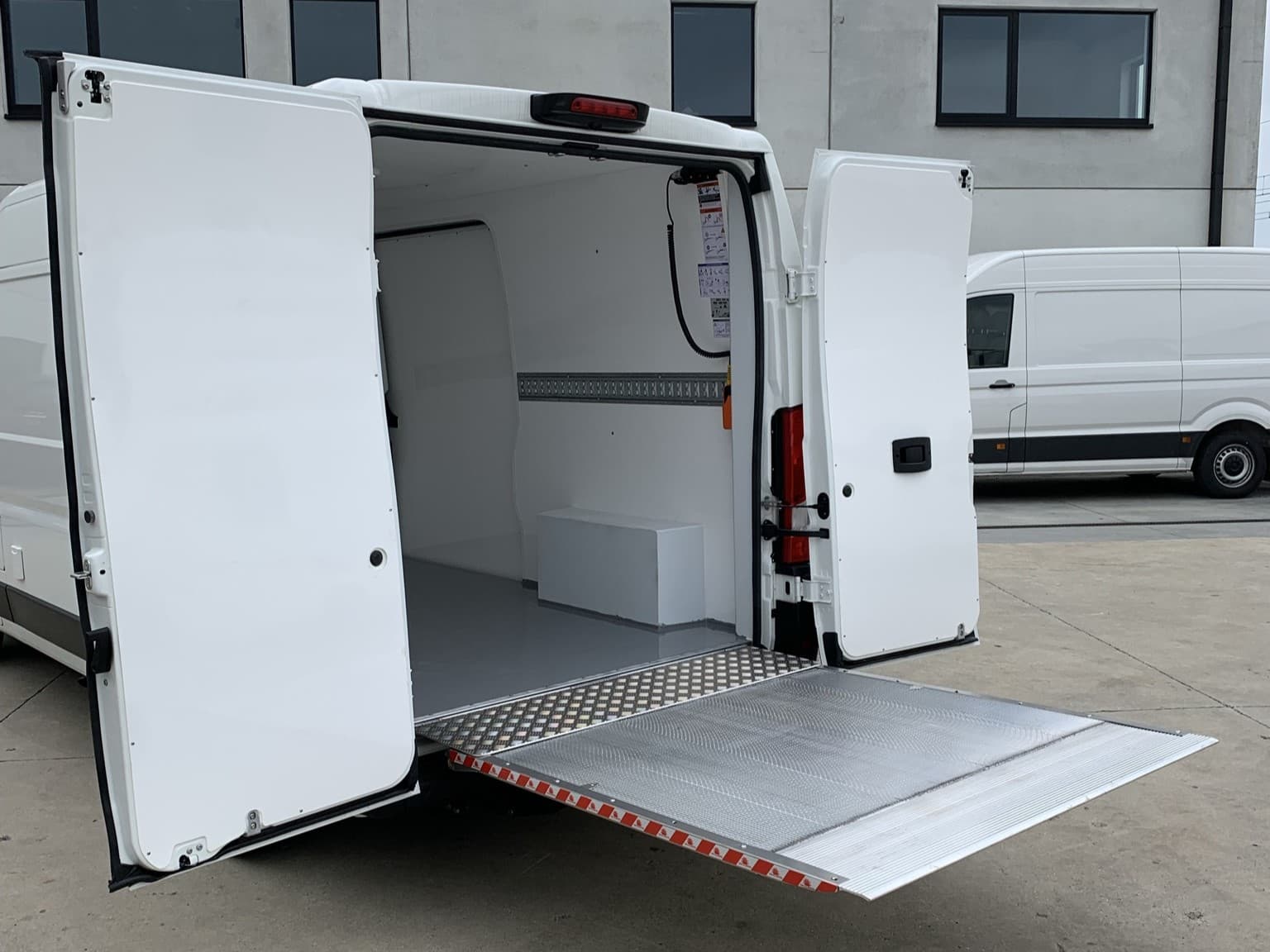 The rear of a finished refrigerated vehicle with the doors open, a white load space and a lowered tail lift