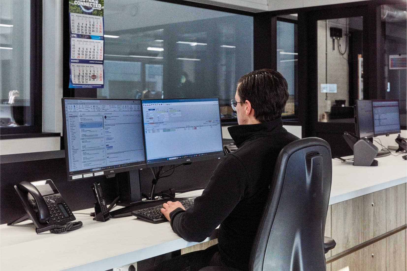 A Westcool planner at a desk with two screens, looking out over the workshop