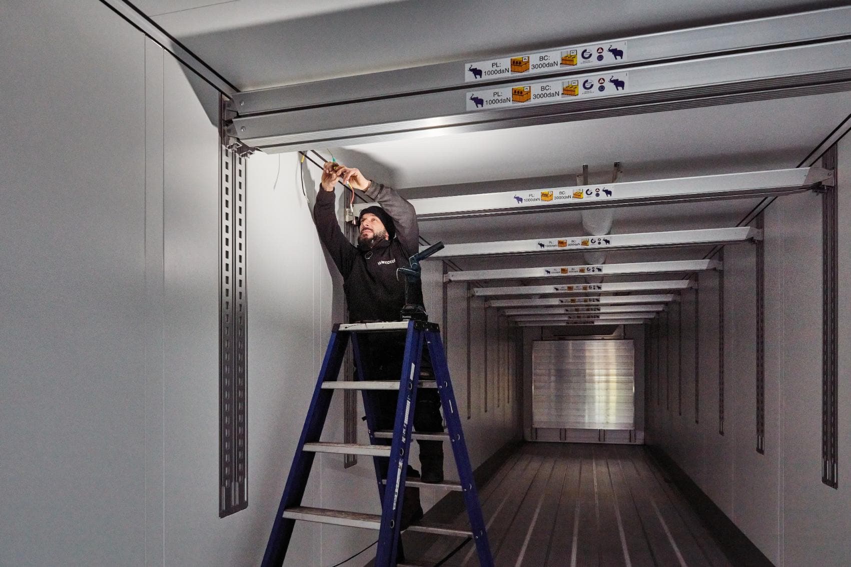 A Westcool technician on a ladder wiring the ceiling of an insulated body