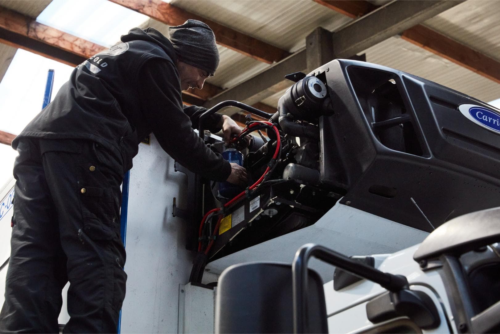 A Westcool technician leaning over an opened Carrier refrigeration unit on the roof of a truck