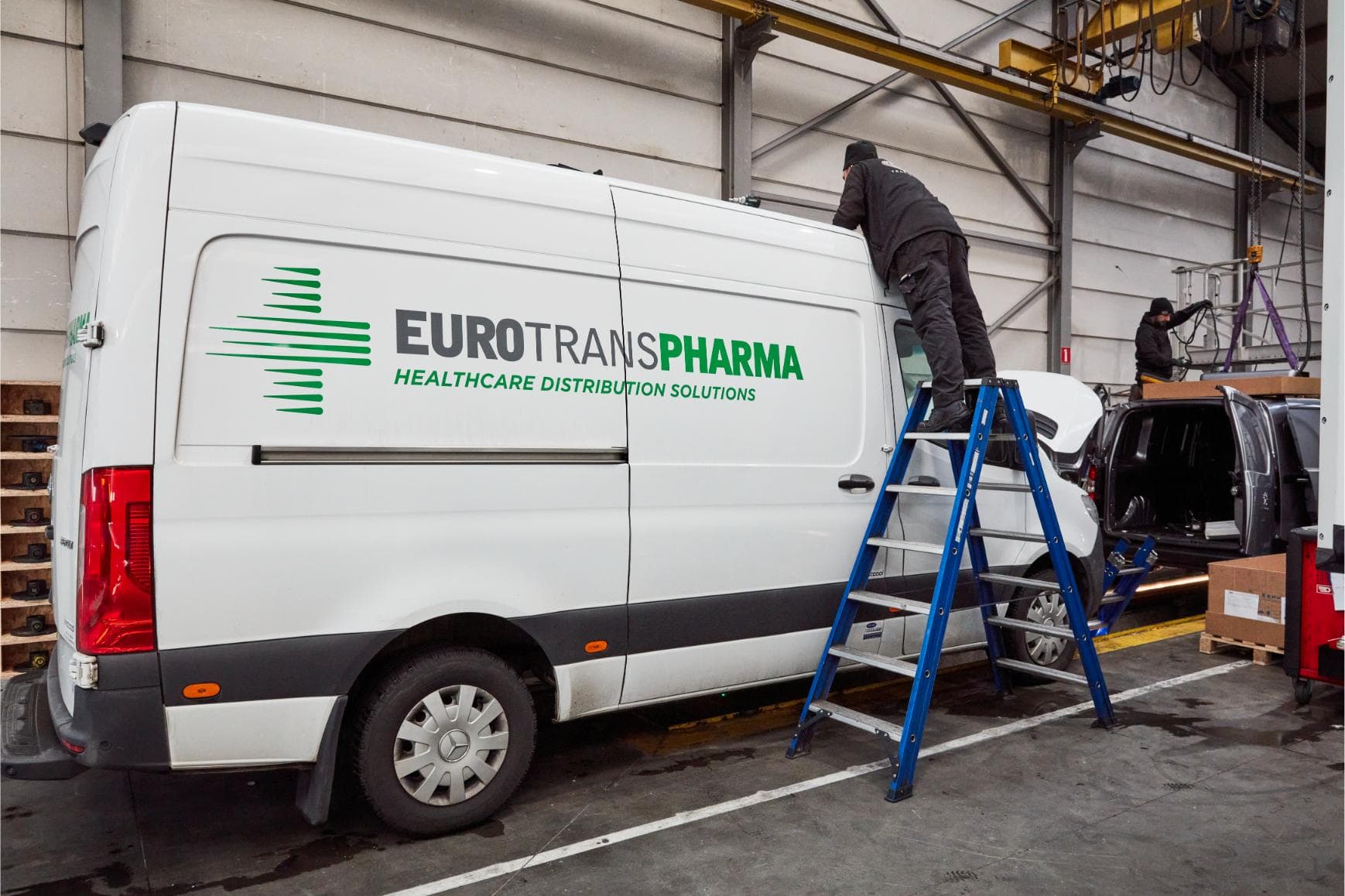 A technician on a ladder at the roof of a white refrigerated van for pharmaceutical transport