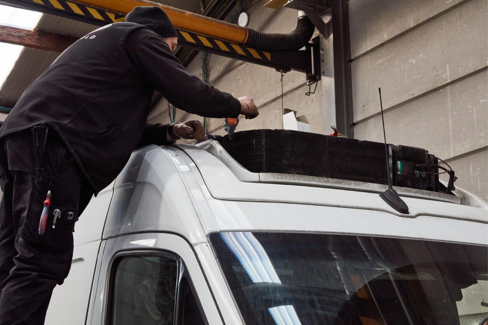 Een carrossier op een trapladder die het dak van een witte bestelwagen opent voor de koelgroep