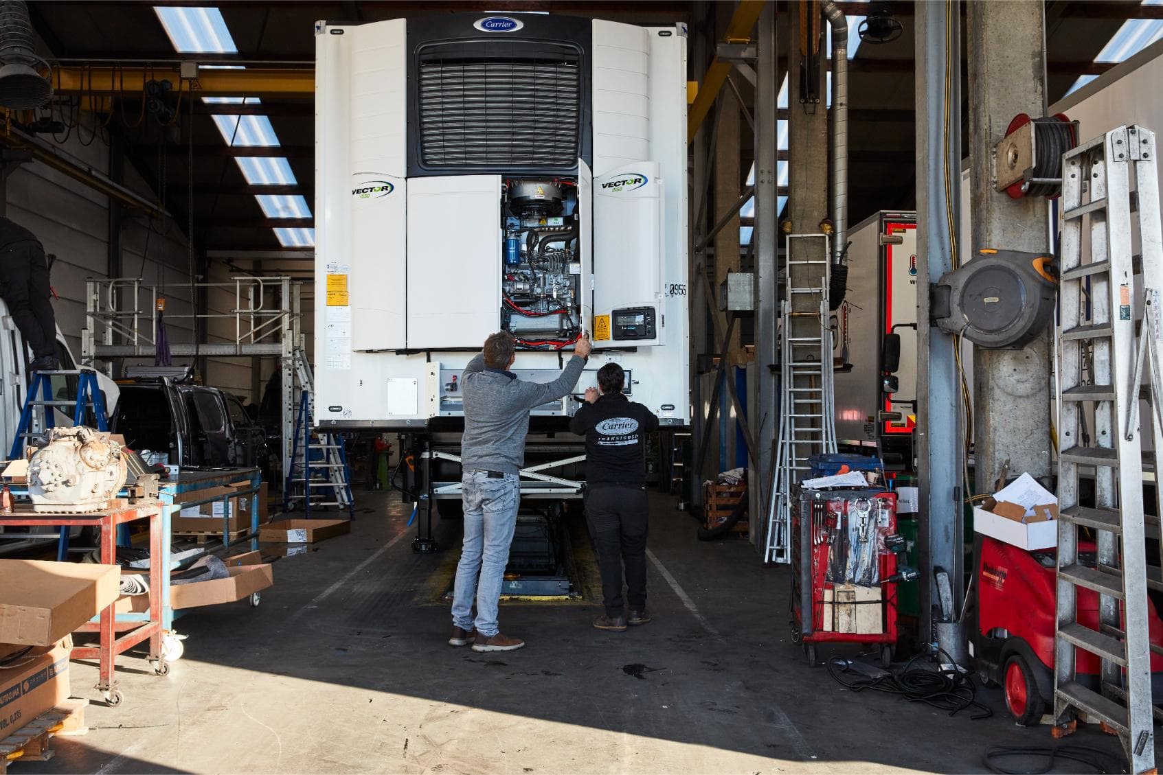 Two technicians beside an opened Carrier Vector 1550 on a trailer in the workshop