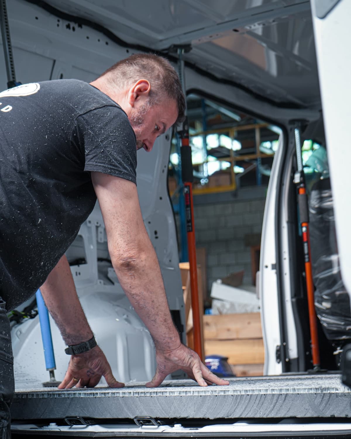 A body builder lays an insulation panel as the floor of a white van's load space
