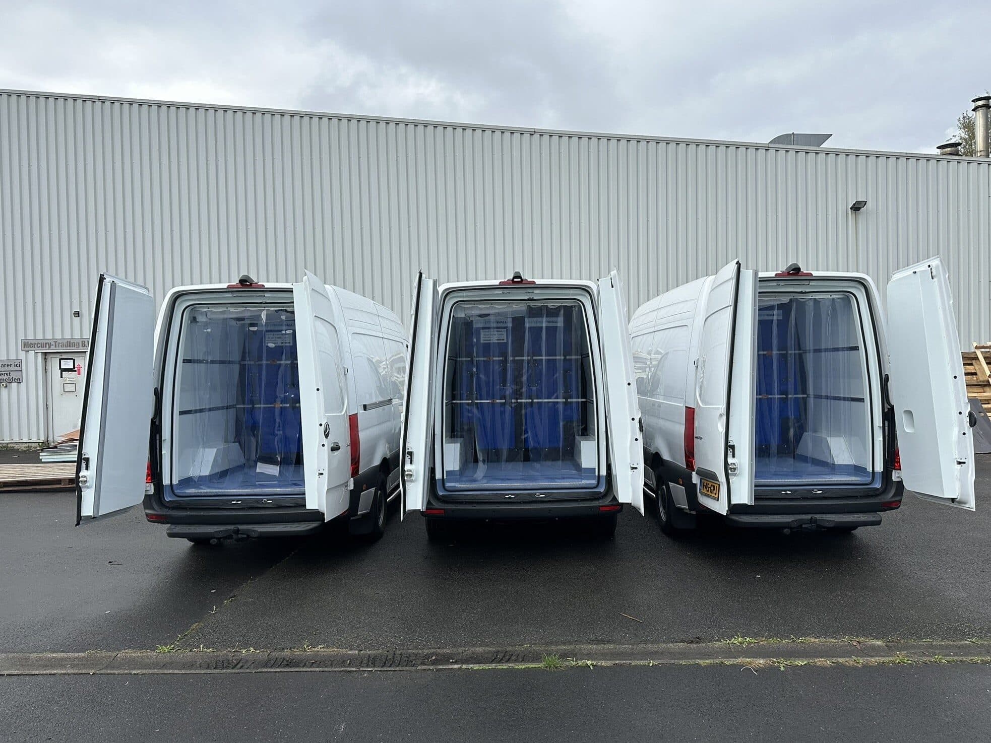 Three white Mercedes Sprinter refrigerated vans with the rear doors open, showing the finished insulation and the blue strip curtains