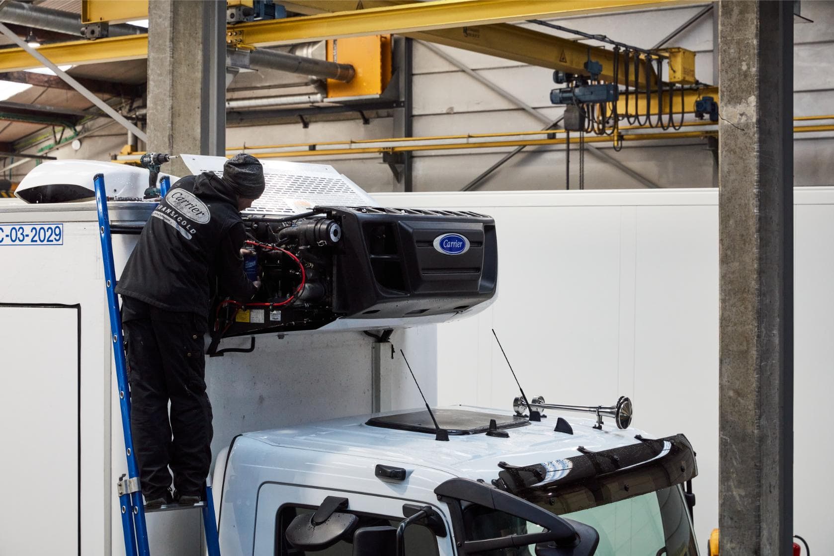 Een technicus die over het dak van een bestelwagen gebogen aan een geopende koelunit werkt