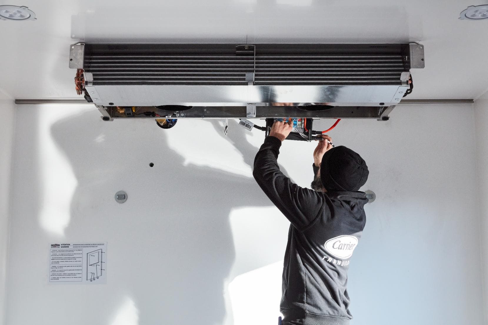 Een technicus die een verdamper aan het plafond van een witte isotherme laadruimte bekabelt
