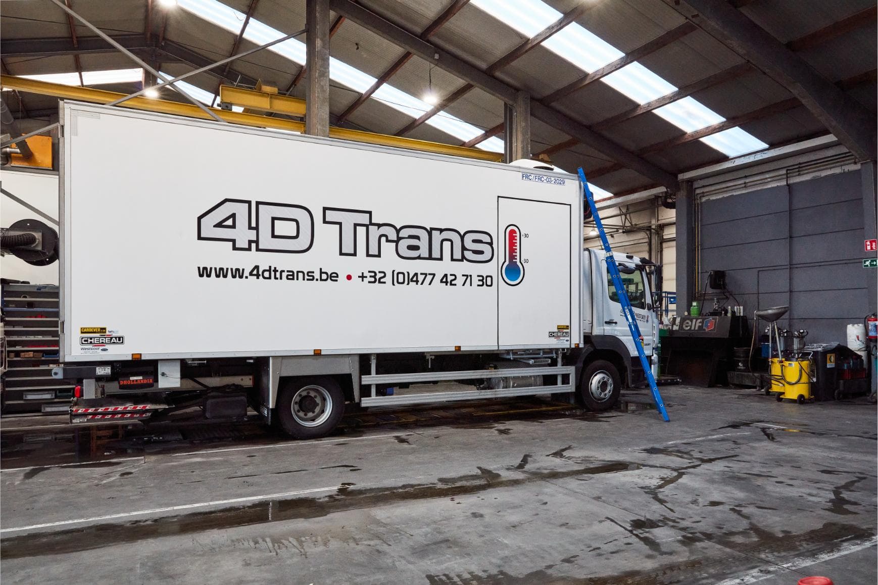 Een Carrier-technicus op een ladder bij een geopende koelgroep op het dak van een vrachtwagen in de werkplaats