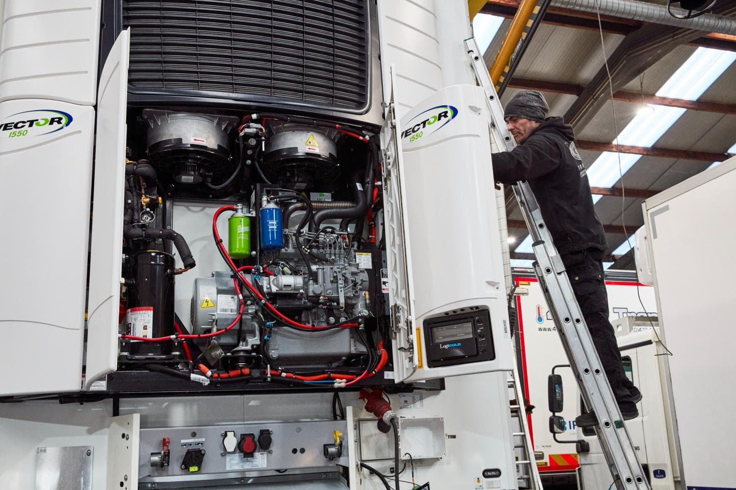 Een geopende Carrier Vector 1550 opleggerunit in de werkplaats, met een technicus op een ladder ernaast